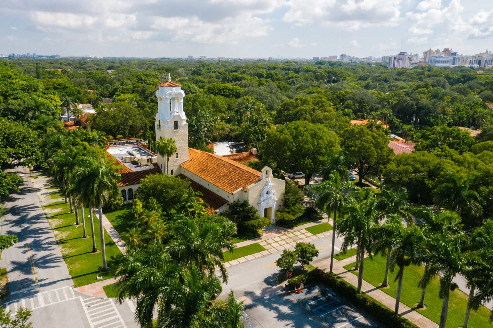 Aerial view of Coral Gables with a Mediterranean-style church, red tile roofs and tree canopy