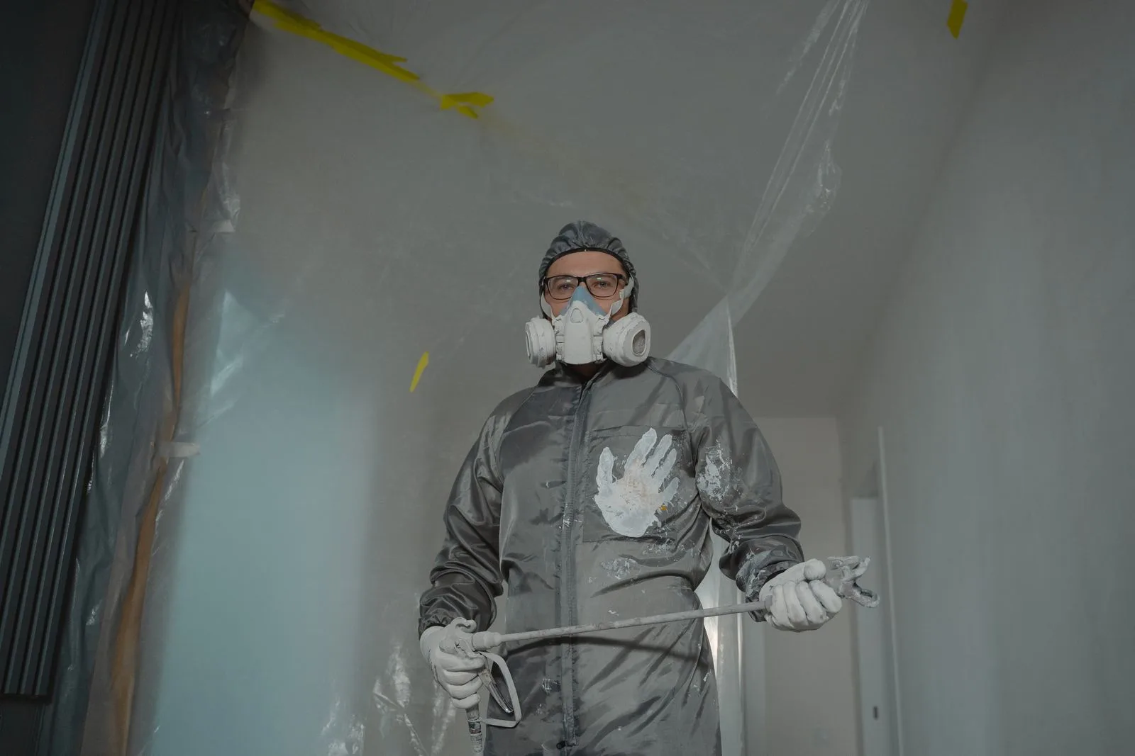 Worker in a respirator and protective suit inside a plastic-sheeted room